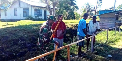 Jalin Kebersamaan, Babinsa Bantu Buat Pagar Balai Kampung Asarkir